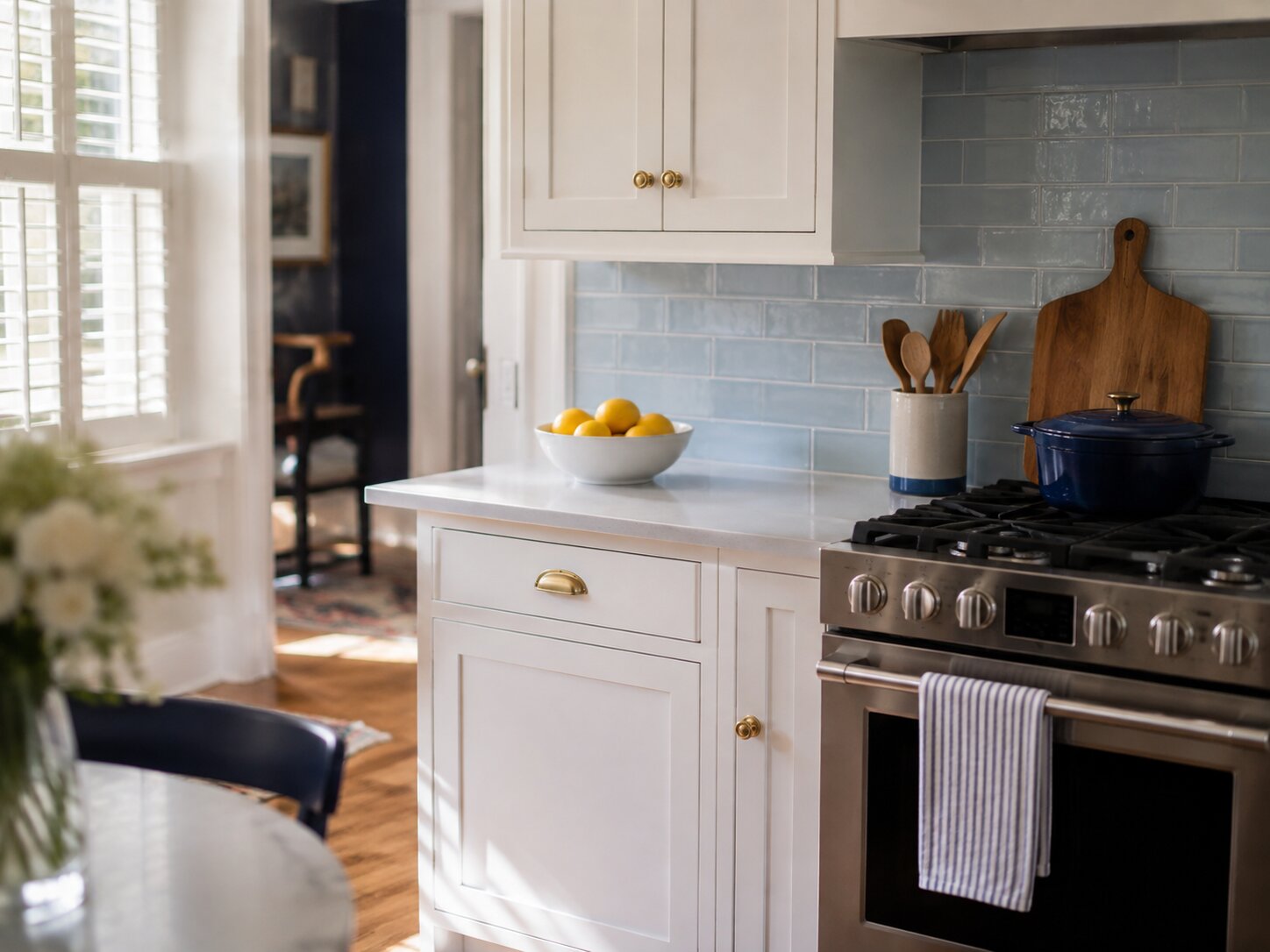 A tidy white kitchen with a pale blue tile backsplash, brass hardware, and a bowl of lemons on a clear counter